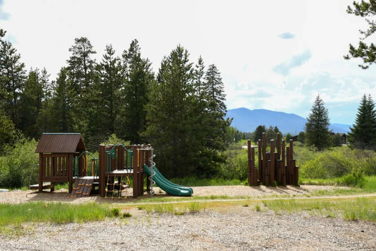 A joyful playground area with modern play structures and slides, nestled among trees with a scenic mountain backdrop. The area is lively, supporting family activities and outdoor enjoyment.