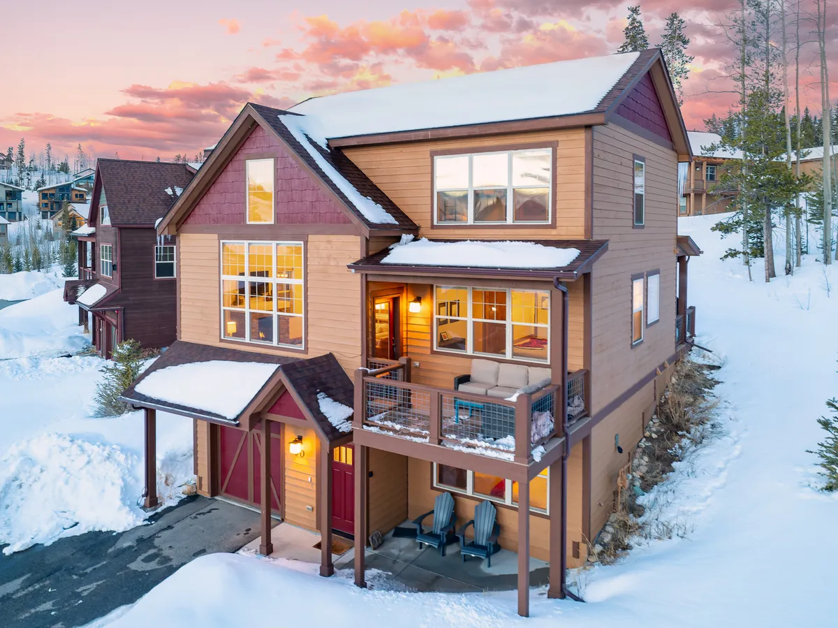 A welcoming exterior view of the home's snow-covered porch, featuring large windows, a balcony seating area, and a warmly lit entrance—suggesting comfort and relaxation after outdoor adventures.