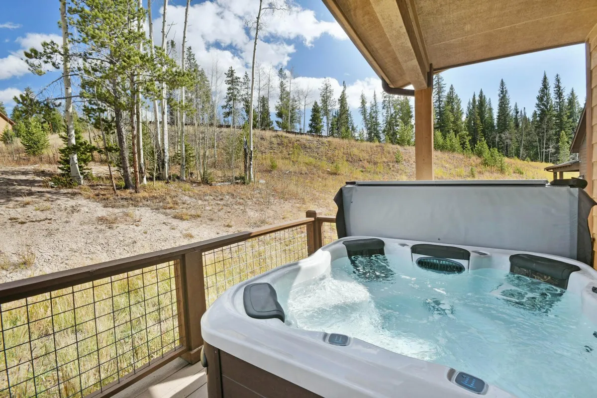 A private hot tub nestled amidst trees, offering a peaceful vantage point for stargazing or morning coffee. The natural landscape and serene mood invite relaxation and connection with nature.