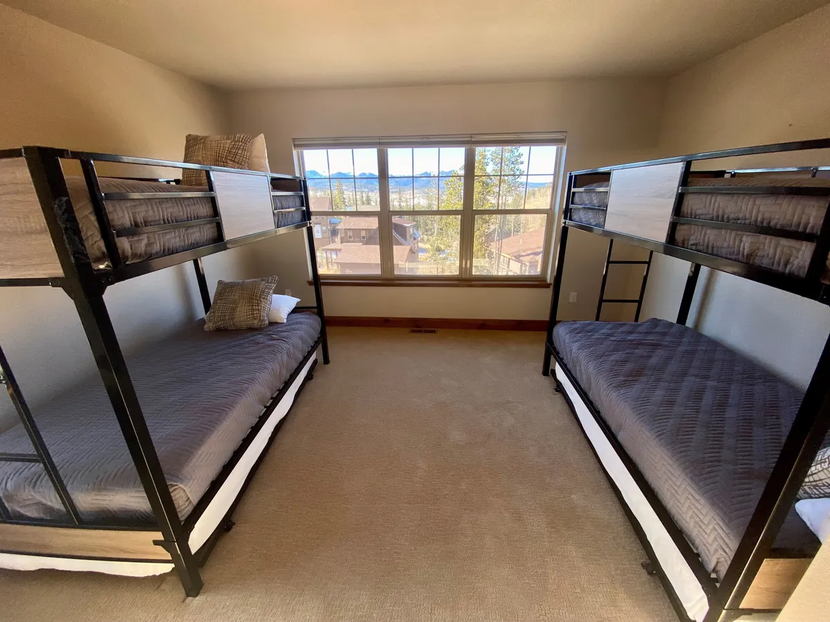 A cozy bunkroom with two stacked bunk beds, decorative pillows, and a large window that offers mountain views. The space feels inviting and playful—ideal for children or friends sharing the space.