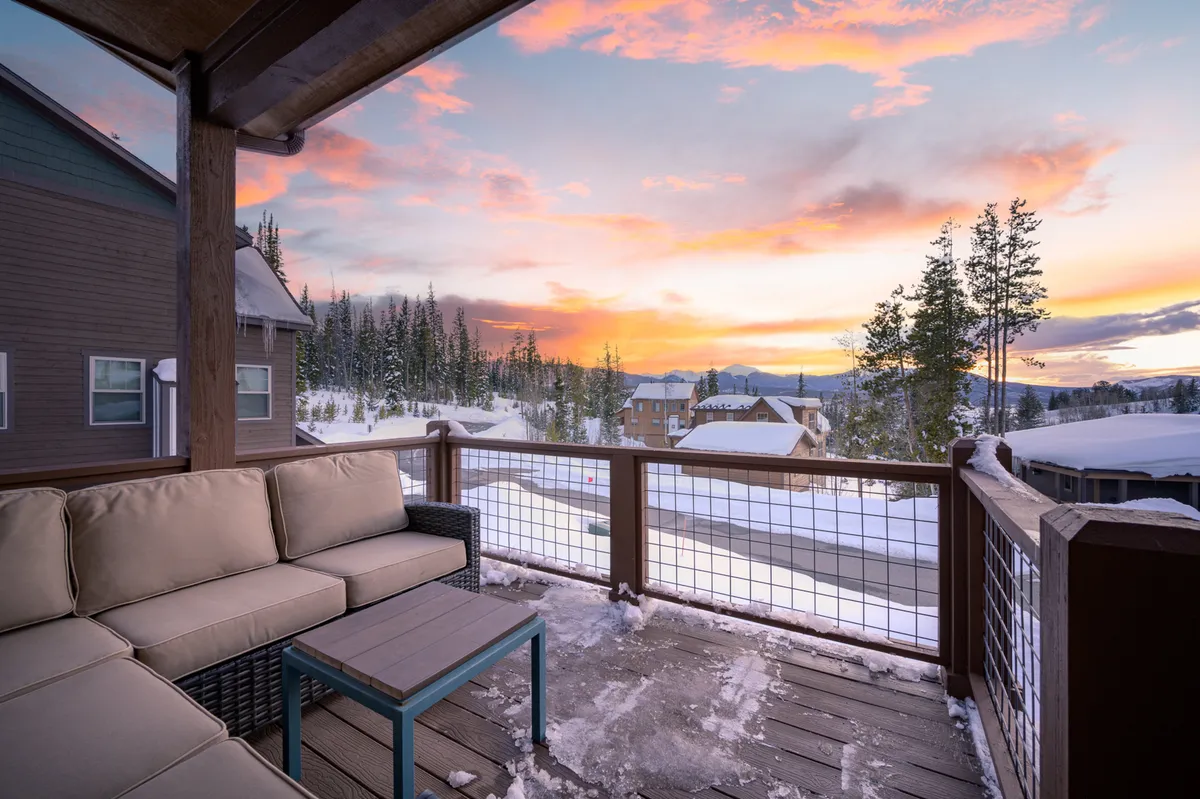 An outdoor seating area set against a snow-covered landscape and a colorful sunset sky. The cozy sectional invites guests to unwind with a warm drink while enjoying mountain vistas and the changing colors of the evening.