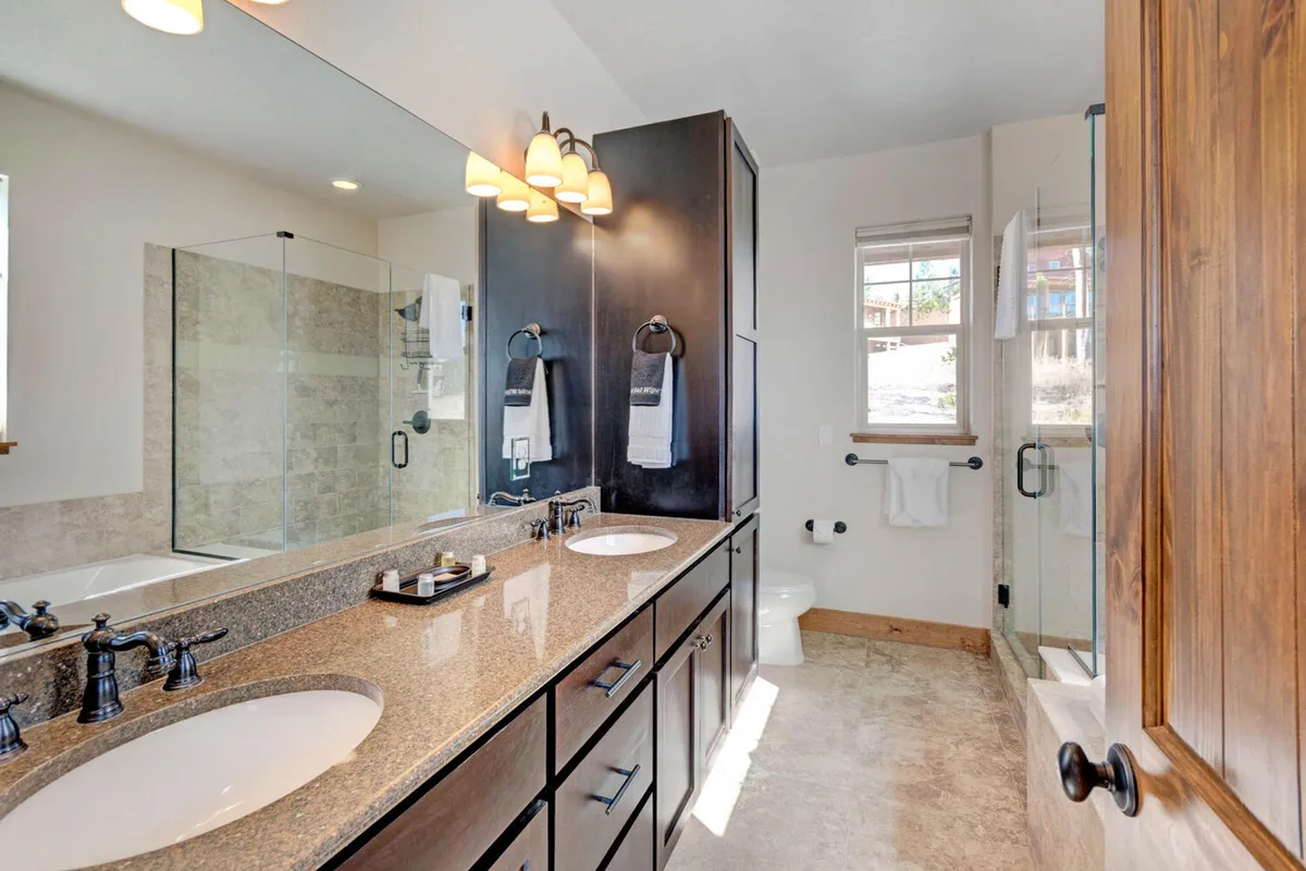 A refreshing bathroom with a double vanity, large mirror, and glass shower enclosure. The space is bright and serene, reflecting a spa-inspired environment with room for shared routines and self-care.