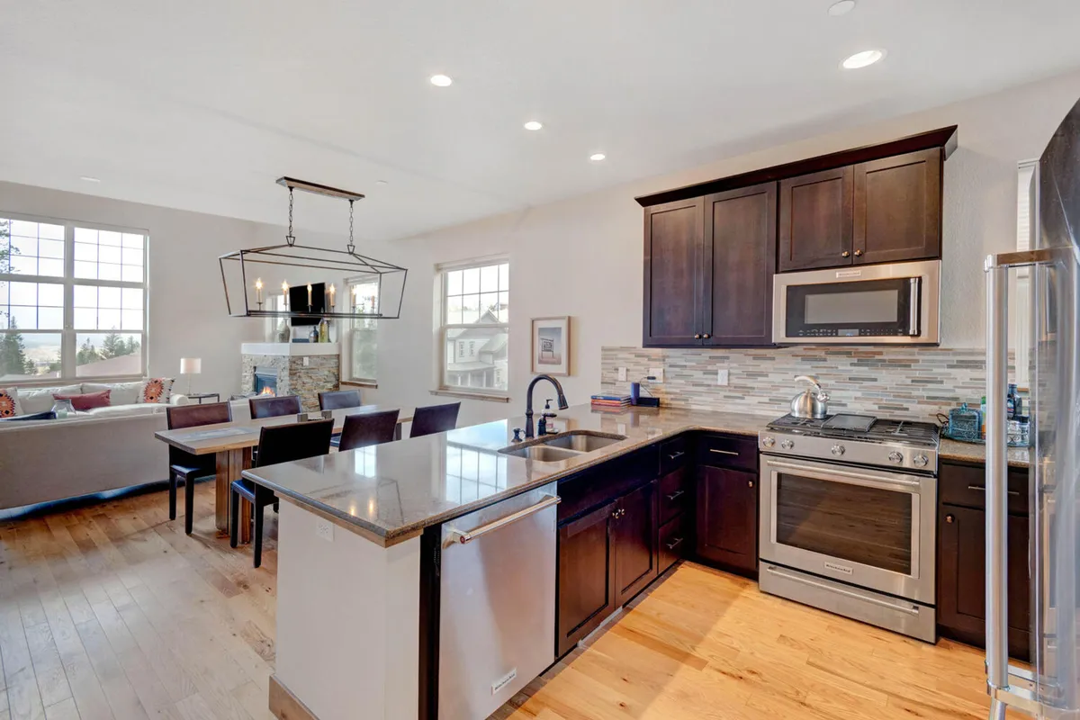 An open layout tying together the kitchen island, dining table, and large windows that bathe the space in natural light. It visually connects the areas for cooking, eating, and gathering, with a welcoming and cozy atmosphere.