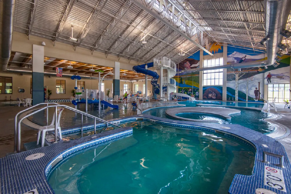 An energetic indoor scene at a recreation center, featuring vibrant water slides, swimming pools, and children playing under colorful murals. Families are gathered for fun water activities, laughter, and memorable moments, all in a lively and safe indoor environment.