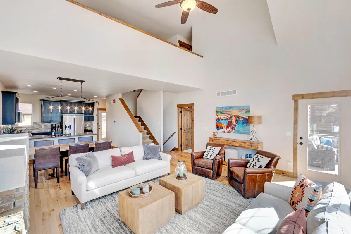 A welcoming living space with a cozy sofa, dual wooden coffee tables, modern art on the wall, and a staircase leading up to a loft area. The arrangement is perfect for conversation, casual board games, or transitioning up to the flexible loft space described in the section.